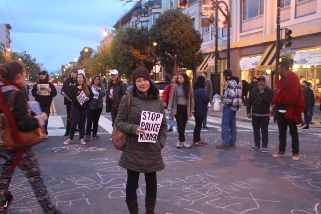Protestor stands in the street holding a placard. Photo by Sana Saleem